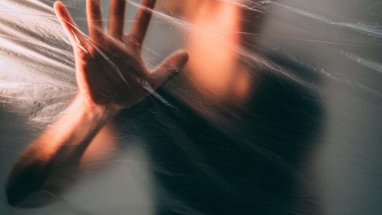 A man behind a plastic bag touching it with his palm