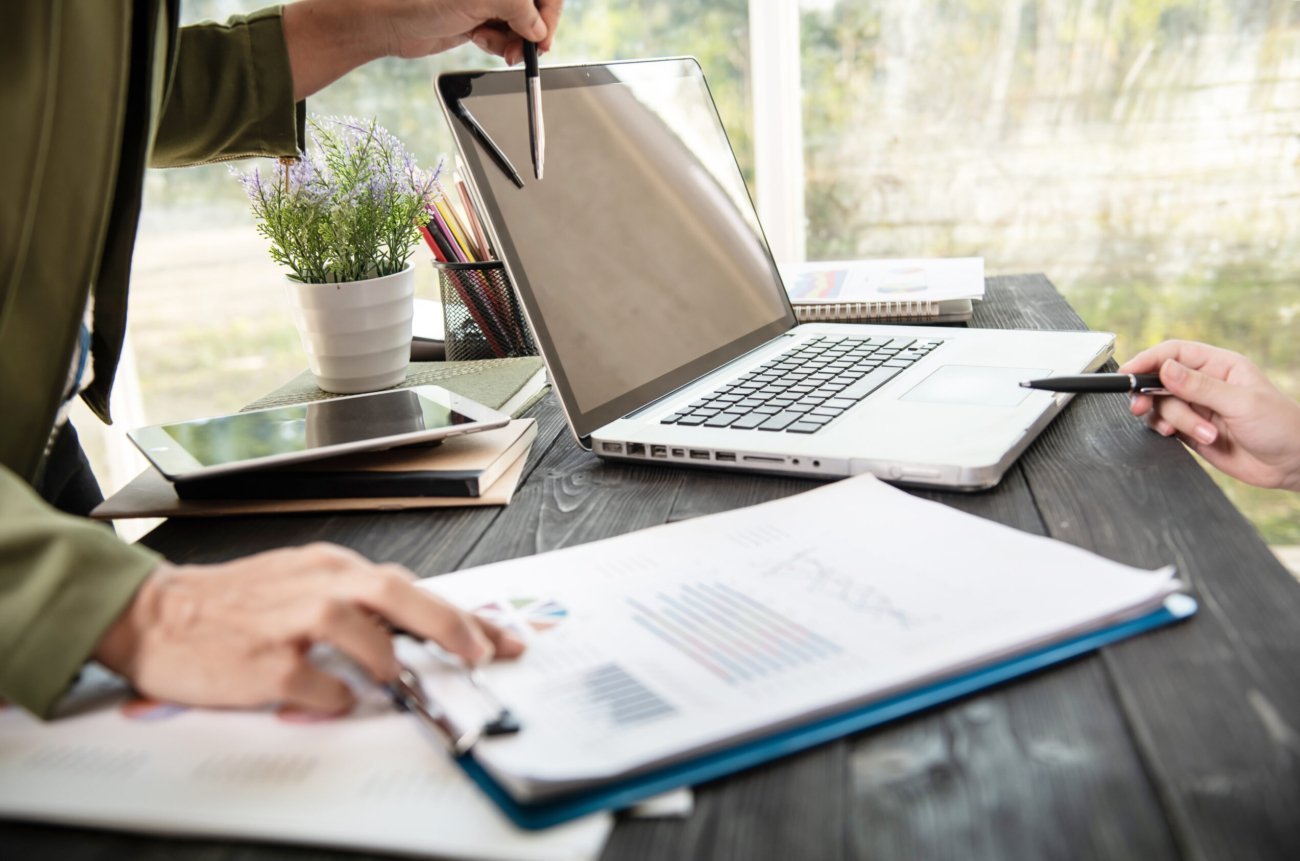 business woman hands using laptop computer placed on messy office desktop. teamwork with business people analysis cost graph on desk at meeting room.