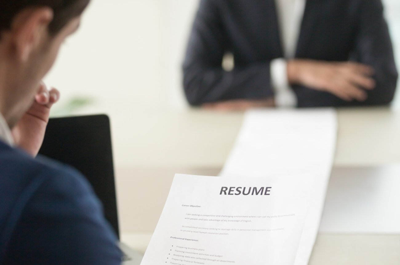 Back view of employer reading resume focus on document, job applicant waiting for hiring decision at desk on background. Hiring manager studying long list of candidates achievements and experiences